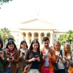 Jóvenes mirando móviles frente a edificio clásico