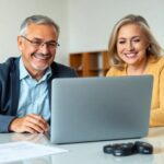 Pareja madura sonriendo frente a portátil en oficina.
