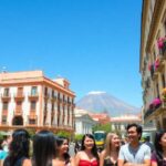 Grupo de personas en plaza con edificio y volcán.