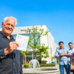 Hombre sonriendo con documento frente a oficina.