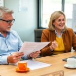 Dos personas trabajando en oficina con documentos y computadora.