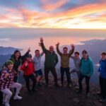 Grupo sonriendo al amanecer en la cima montañosa.