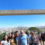 Grupo de personas ante marco con ciudad de fondo.